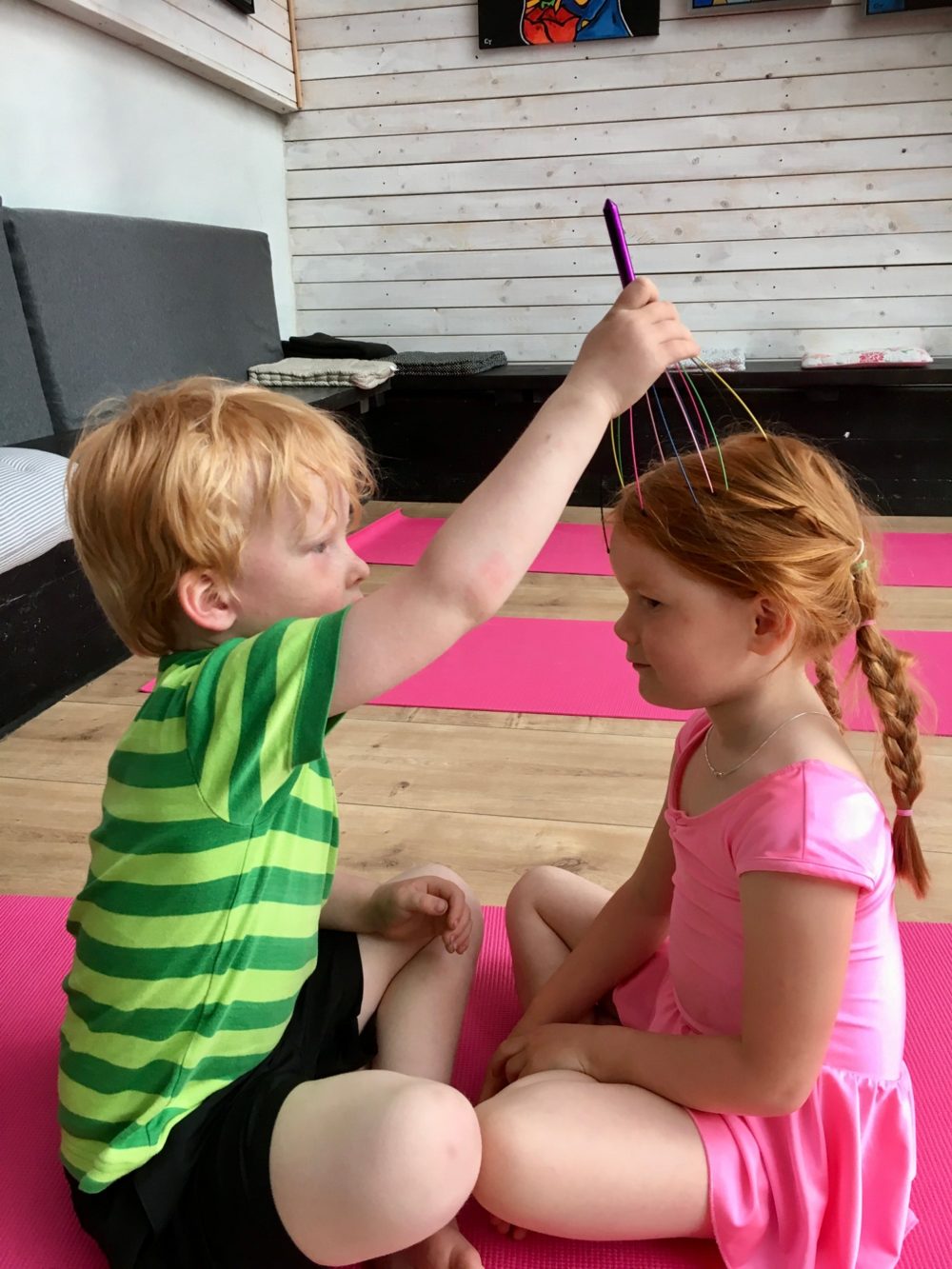 To børn sidder over for hinanden på yogamåtter, mens det ene giver det andet en hovedmassage