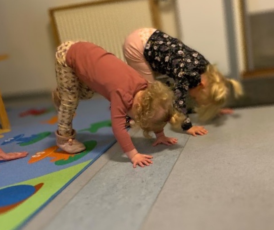 To børn i hunden med hovedet nedad på et farverigt legetæppe
